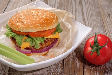 The hamburger lies on an old wooden table. On the table is a hamburger, tomato sauce, cherry tomatoes, a jar of spices.