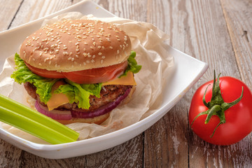 The hamburger lies on an old wooden table. On the table is a hamburger, tomato sauce, cherry tomatoes, a jar of spices.
