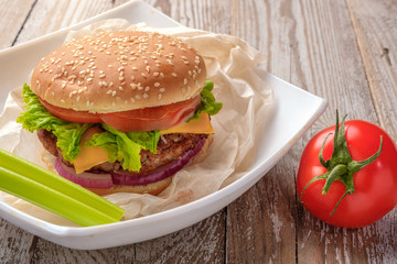 The hamburger lies on an old wooden table. On the table is a hamburger, tomato sauce, cherry tomatoes, a jar of spices.
