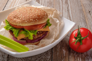 The hamburger lies on an old wooden table. On the table is a hamburger, tomato sauce, cherry tomatoes, a jar of spices.