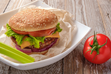 The hamburger lies on an old wooden table. On the table is a hamburger, tomato sauce, cherry tomatoes, a jar of spices.