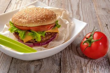 The hamburger lies on an old wooden table. On the table is a hamburger, tomato sauce, cherry tomatoes, a jar of spices.