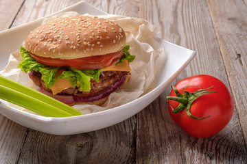 The hamburger lies on an old wooden table. On the table is a hamburger, tomato sauce, cherry tomatoes, a jar of spices.