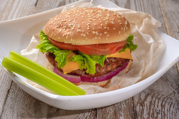The hamburger lies on an old wooden table. On the table is a hamburger, tomato sauce, cherry tomatoes, a jar of spices.