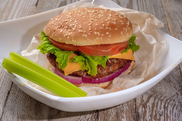The hamburger lies on an old wooden table. On the table is a hamburger, tomato sauce, cherry tomatoes, a jar of spices.