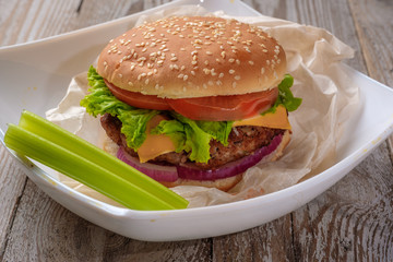 The hamburger lies on an old wooden table. On the table is a hamburger, tomato sauce, cherry tomatoes, a jar of spices.