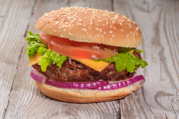 The hamburger lies on an old wooden table. On the table is a hamburger, tomato sauce, cherry tomatoes, a jar of spices.