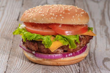 The hamburger lies on an old wooden table. On the table is a hamburger, tomato sauce, cherry tomatoes, a jar of spices.