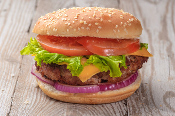 The hamburger lies on an old wooden table. On the table is a hamburger, tomato sauce, cherry tomatoes, a jar of spices.
