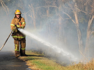 Melbourne, Australia - April 13, 2018: Fire fighter with a hose at a bush fire in an suburban area...