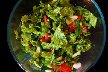Salad with tomatoes, cucumbers, lettuce and green onions. Dark stone background. View from above.