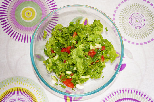 Salad with tomatoes, cucumbers, lettuce and green onions in bowl. Light coloured table on background. View from above.