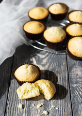 Many cupcakes in molds, one broken, on wooden surface