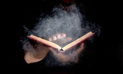 hand holding mysterious old book, white particle and smoke spread from book