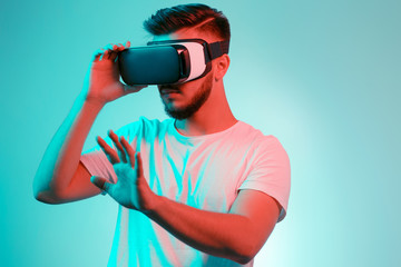 Handsome bearded man trying VR headset and exploring another world on the colorful background. Smartphone using with VR headset.