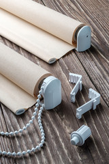 The rolled beige shutters is on a wooden surface. Beige blinds lie on an old wooden table.