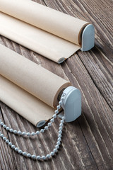 The rolled beige shutters is on a wooden surface. Beige blinds lie on an old wooden table.