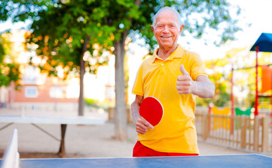 Happy mature man playing table tennis and showing thumb up