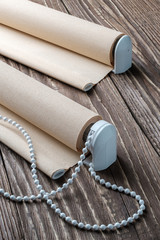 The rolled beige shutters is on a wooden surface. Beige blinds lie on an old wooden table.