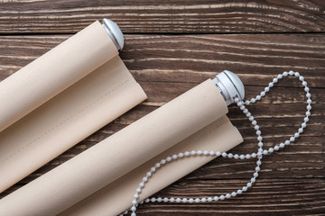 The rolled beige shutters is on a wooden surface. Beige blinds lie on an old wooden table.