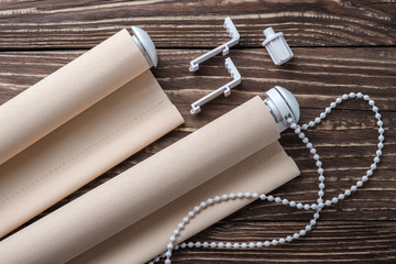 The rolled beige shutters is on a wooden surface. Beige blinds lie on an old wooden table.