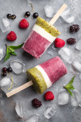 Fototapeta na wymiar Healthy ice cream popsicles with berries, kiwi and yogurt on light concrete background, overhead view