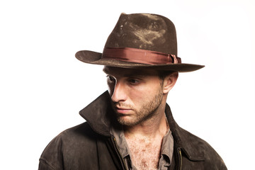 Young sexy  unshaven man in cowboy hat. Indiana Jones image. Stylish dark brown clothes on a white background - obrazy, fototapety, plakaty