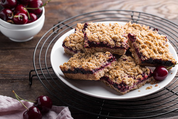 Homemade crumble bars with cherries on rustic wooden background