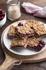 Homemade crumble bars with cherries on rustic wooden background
