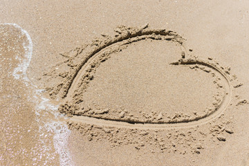 Heart in the sand on the ocean, the sea washed off by a wave.