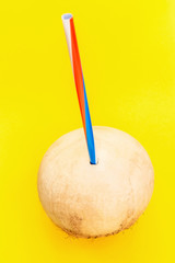 Fresh organic coconut with straw on yellow background