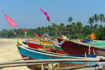 Fototapeta na wymiar Small fishing boats in reggae colors on ocean beach seashore against blue sky. India, Goa, Maharashtra