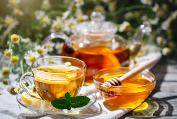 Cup with hot tea with mint and a thyme on a wooden table in a summer garden.