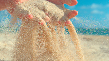 CLOSE UP: Unknown young woman scattering white sand between her fingertips.