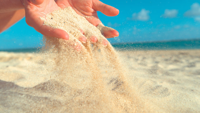 CLOSE UP: Unknown young woman lets hot sand fall through her gentle fingers.