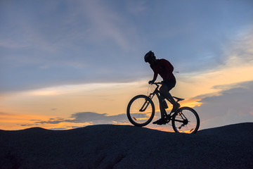 Fototapeta na wymiar silhouette of a man riding a mountain bike up a hill, extreme sport mountain biker