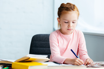 adorable red haired schoolgirl sitting at desk and studying at home