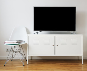 Wide screen TV on white stand near light wall