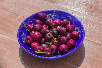 blue plate of ripe sweet cherry on  wooden table