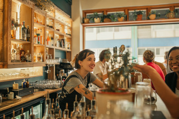 Smiling female bartender talking with customers at a bar counter - obrazy, fototapety, plakaty