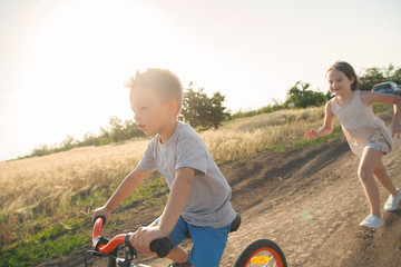 Boy and girl in the field. The boy is riding a bicycle, and the girl is running alongside. A...