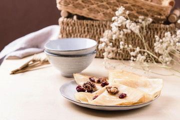 Homemade gluten free rice crepes or pancakes served with dried cranberries and walnuts on wooden table. Healthy breakfast