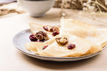 Homemade gluten free rice crepes or pancakes served with dried cranberries and walnuts on wooden table. Healthy breakfast