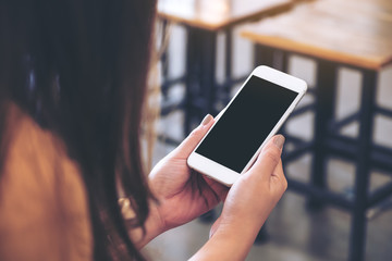 Mockup image of a woman holding white mobile phone with blank black desktop screen in cafe