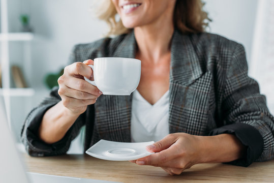 cropped image of attractive businesswoman sitting with cup of coffee at table in office