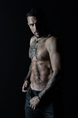 Fototapeta na wymiar Bearded man shirtless with fit torso. Man with tattoo design on skin. Fashion model buckle leather belt in jeans. Sportsman with six pack and ab. Fitness with sport and bodycare, vintage filter