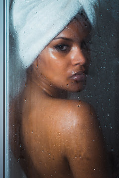 Portrait of young woman standing behind steamy shower glass