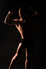 Fototapeta na wymiar Silhouette of muscular athlete, darknes and light. Man with sexy fit body isolated on black background. Bodybuilder with bare torso. fitness model showing strong muscles, sport and health concept