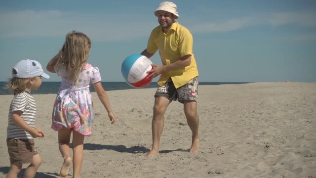 Father enjoying playing ball with young little kid on beach. Family Summer Beach Vacation. Slow Motion. Children play with dad on the beach.