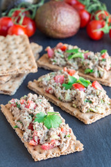 Salad with tuna, avocado, tomatos, coriander and lemon juice, served on crispbread, ingredients on background, vertical